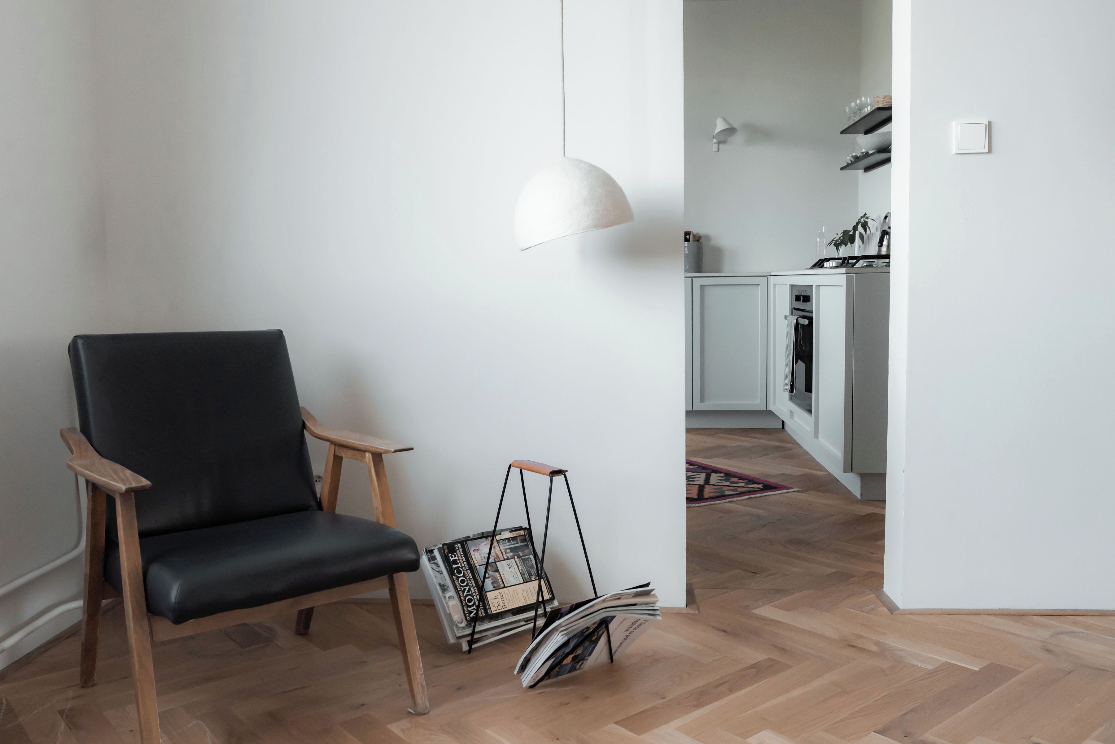 Een moderne woonkamer met een zwarte leren fauteuil, een hanglamp en een tijdschriftrek.