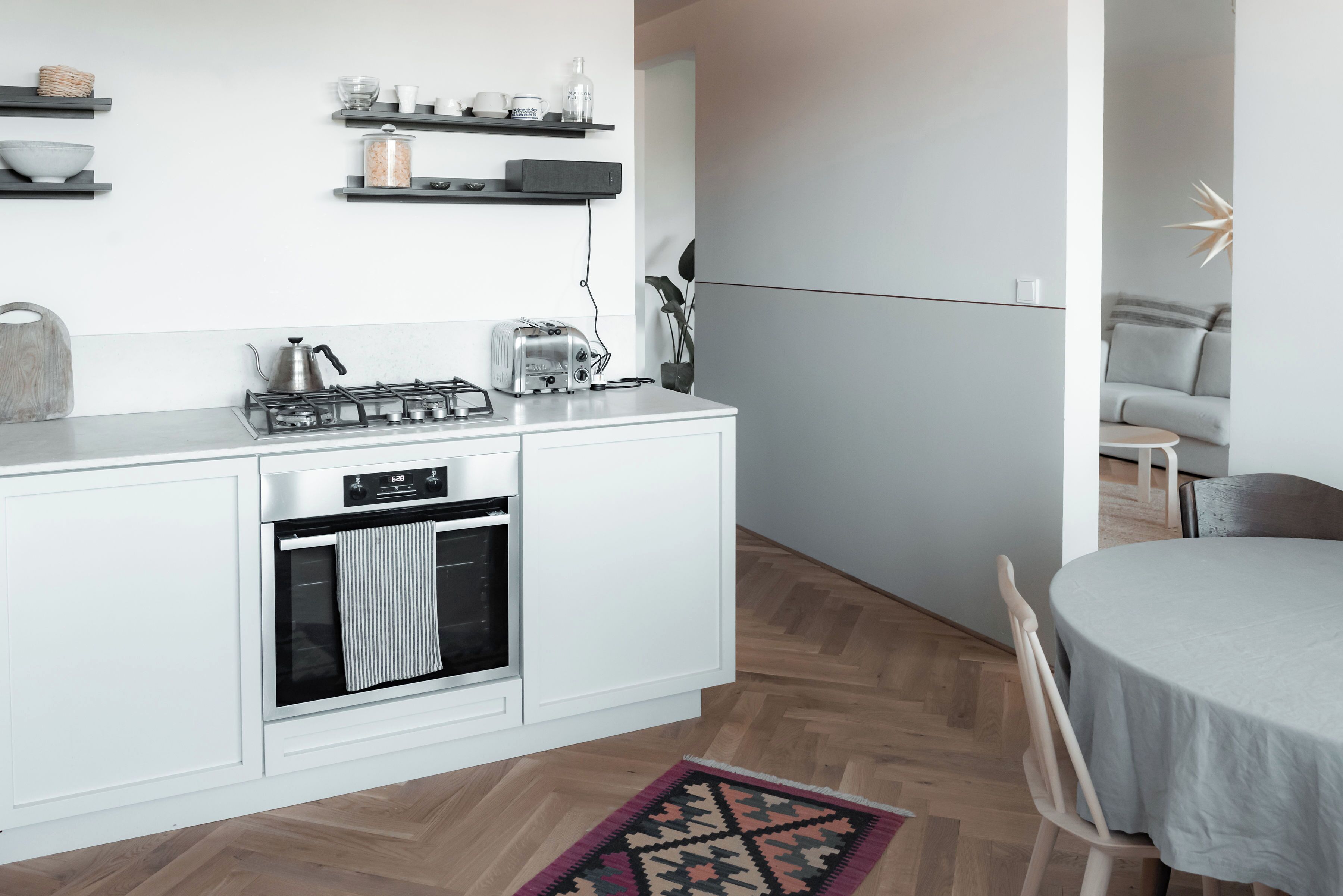 A modern kitchen with white cabinetry, a built-in oven, and a gas stove. There is a dining area with a round table and chairs.
