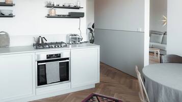 A modern kitchen with white cabinetry, a built-in oven, and a gas stove. There is a dining area with a round table and chairs.