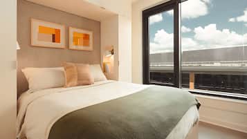 Ein modernes Hotelzimmer mit einem großen Bett, Blick auf das Flughafengelände und zwei gerahmten Kunstwerken an der Wand.
