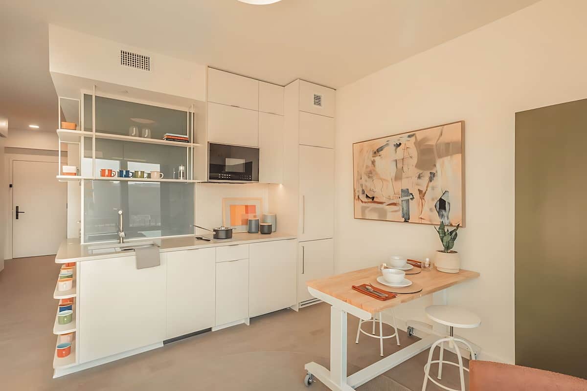 A modern kitchen with white cabinetry, a microwave, and a dining area with stools.
