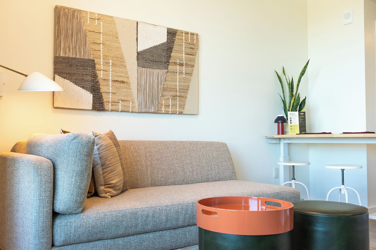 A modern living room with a grey sofa, a coffee table, a lamp, and a wall-mounted abstract artwork.