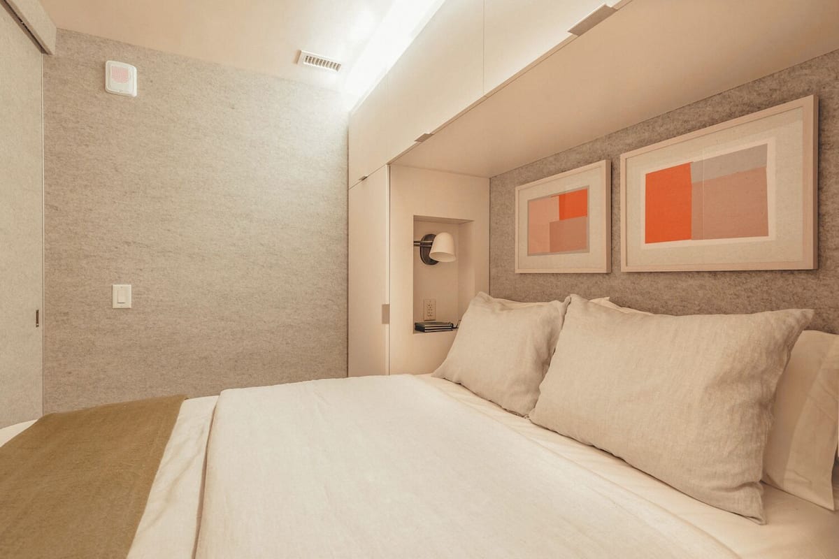 A hotel room with a bed, a nightstand, a lamp, and two framed abstract paintings on the wall.