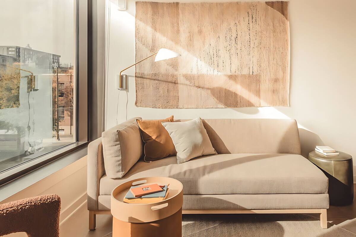 A modern living room with a large window, a sofa, a side table, and a wall-mounted lamp.