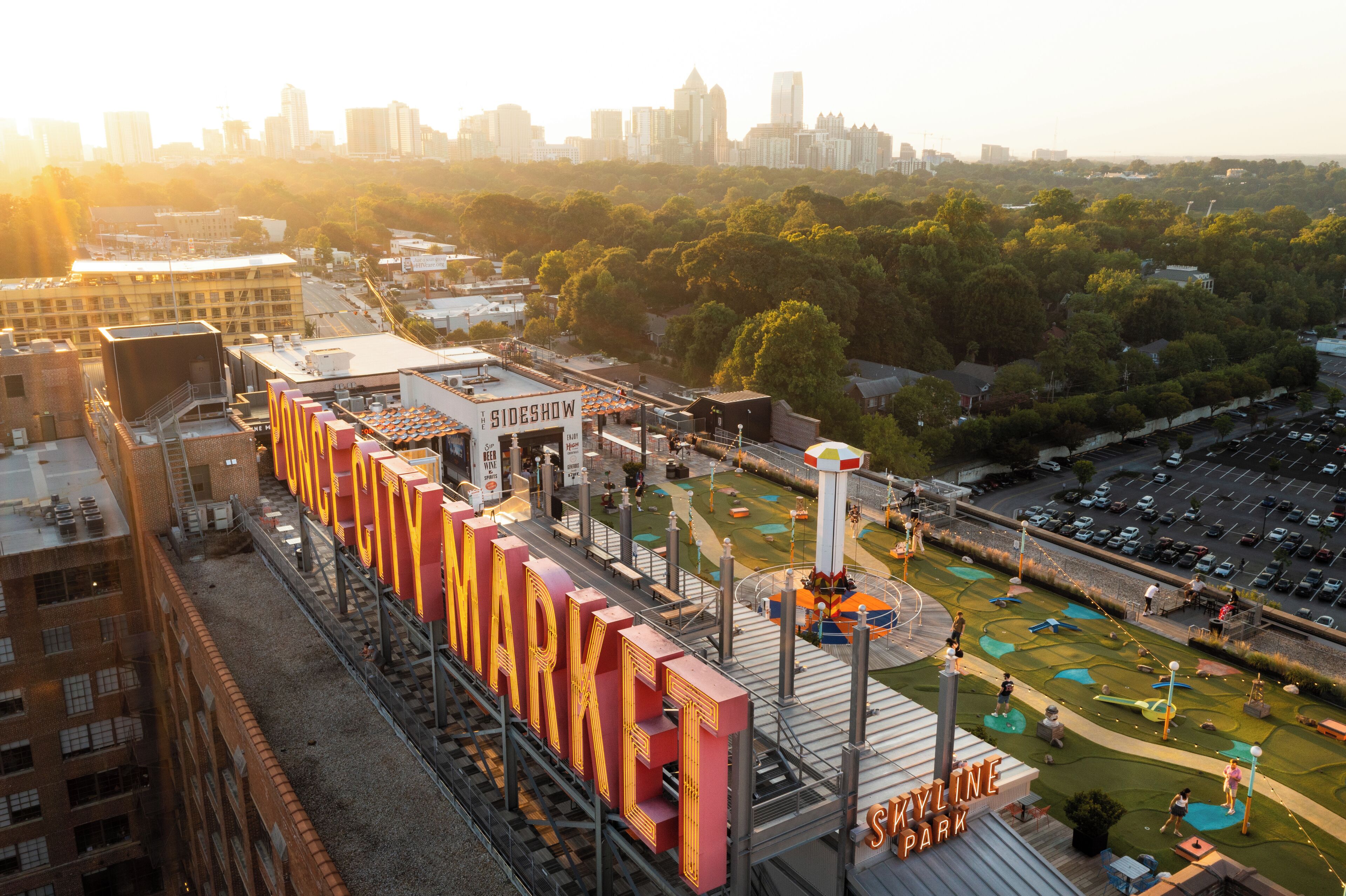 Un mercado al aire libre grande con un letrero llamativo, rodeado de estacionamiento y un horizonte urbano de fondo.