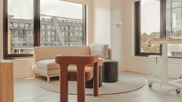 Een moderne woonkamer met een bank, een krabpaal, een kleine tafel en een stadsgezicht door grote ramen.