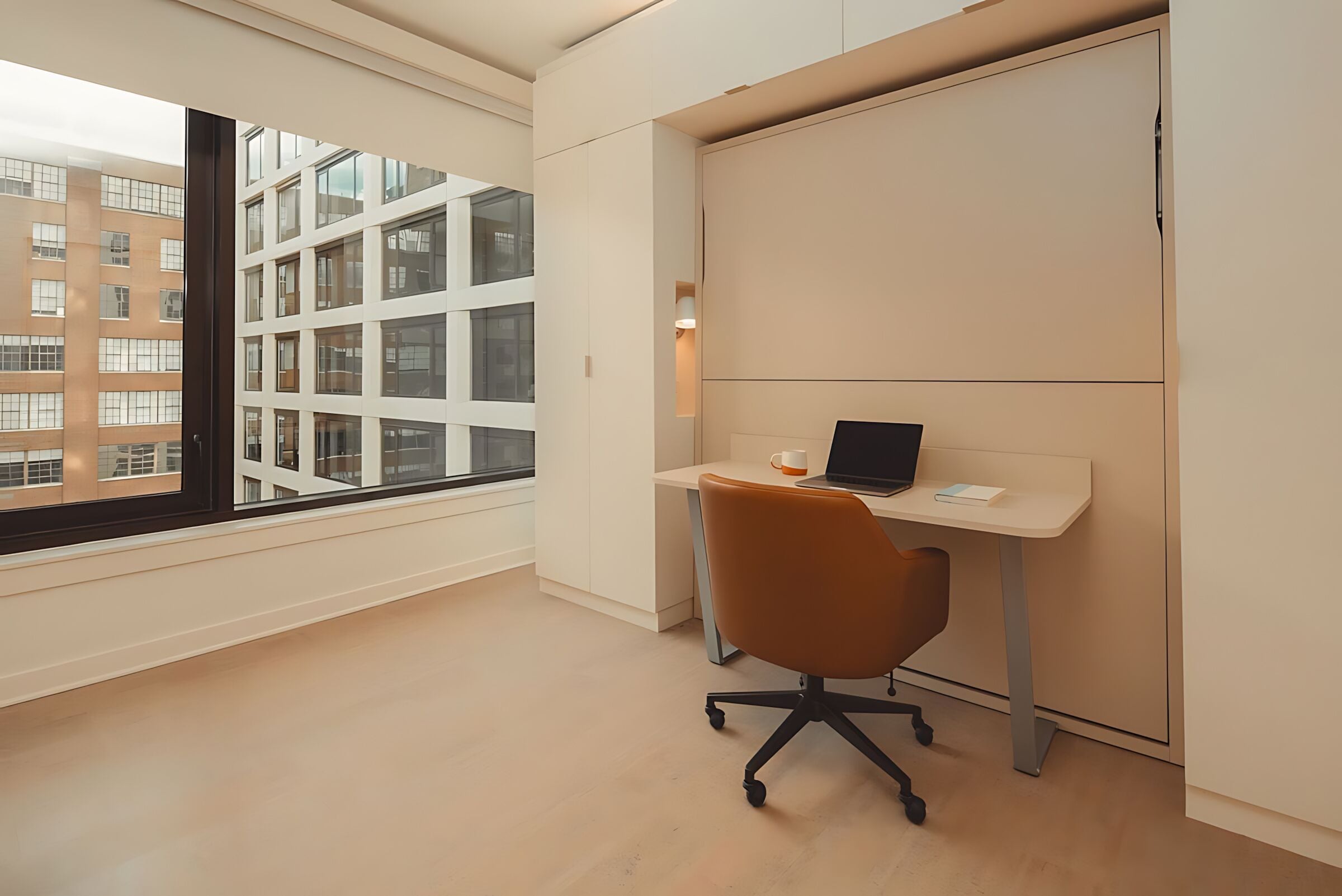 A modern office space with a large window, a desk with a laptop, and a chair.