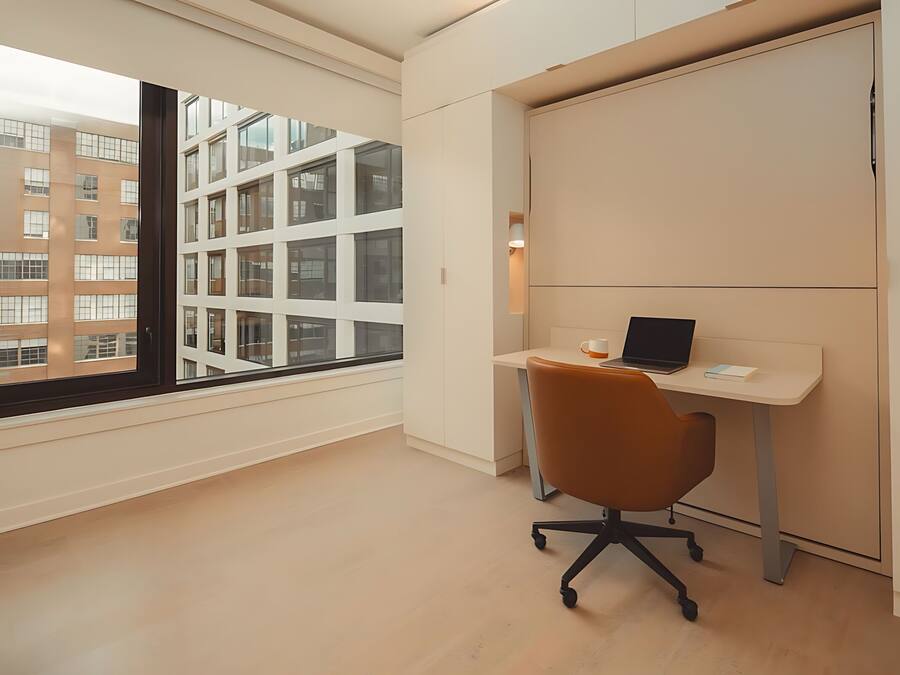 A modern office space with a large window, a desk with a laptop, and a chair.