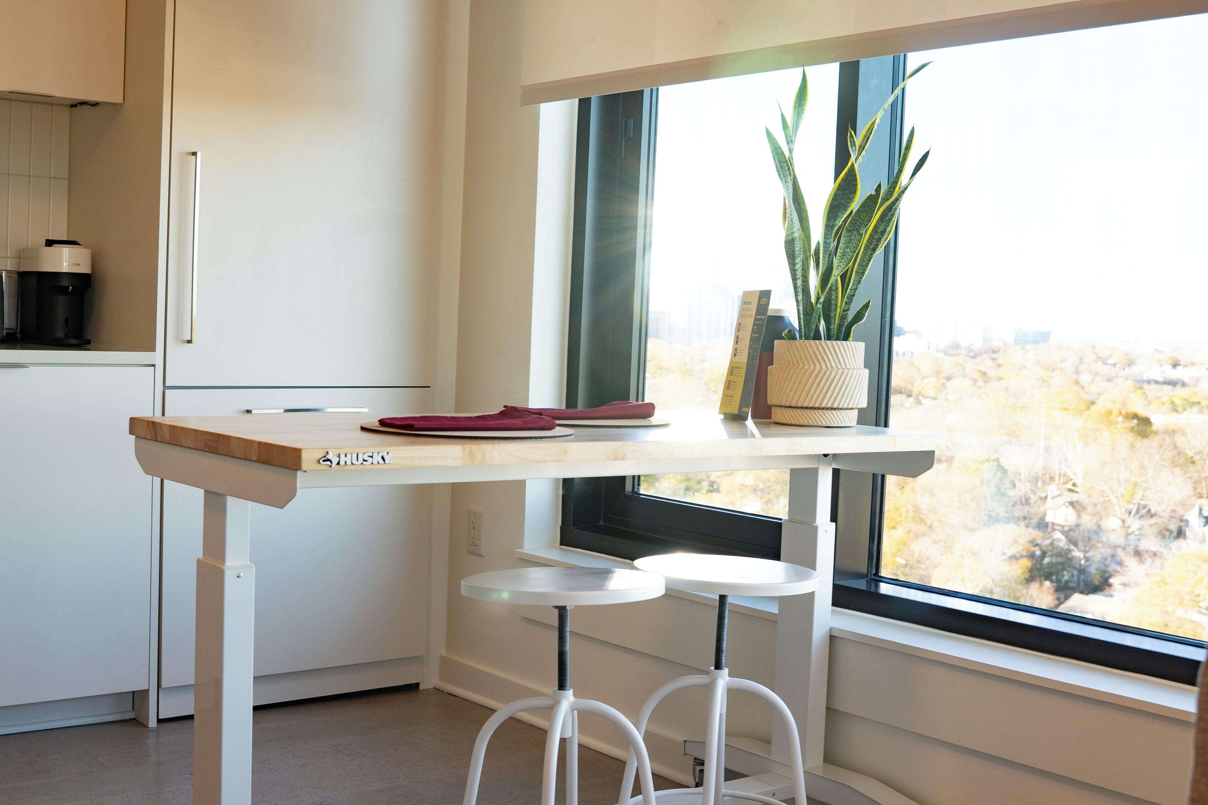 A kitchen with a wooden countertop, two stools, a window with a view of trees, and a potted plant.
