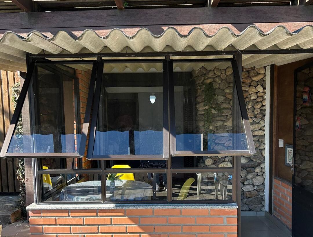 Un restaurante con fachada de ladrillo, pared de piedra y un amplio ventanal con toldo metálico.