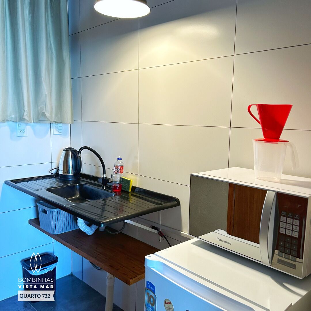 A compact kitchen with a sink, kettle, and microwave. A red funnel and a clear cup are on the counter.