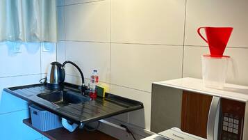 A compact kitchen with a sink, kettle, and microwave. A red funnel and a clear cup are on the counter.
