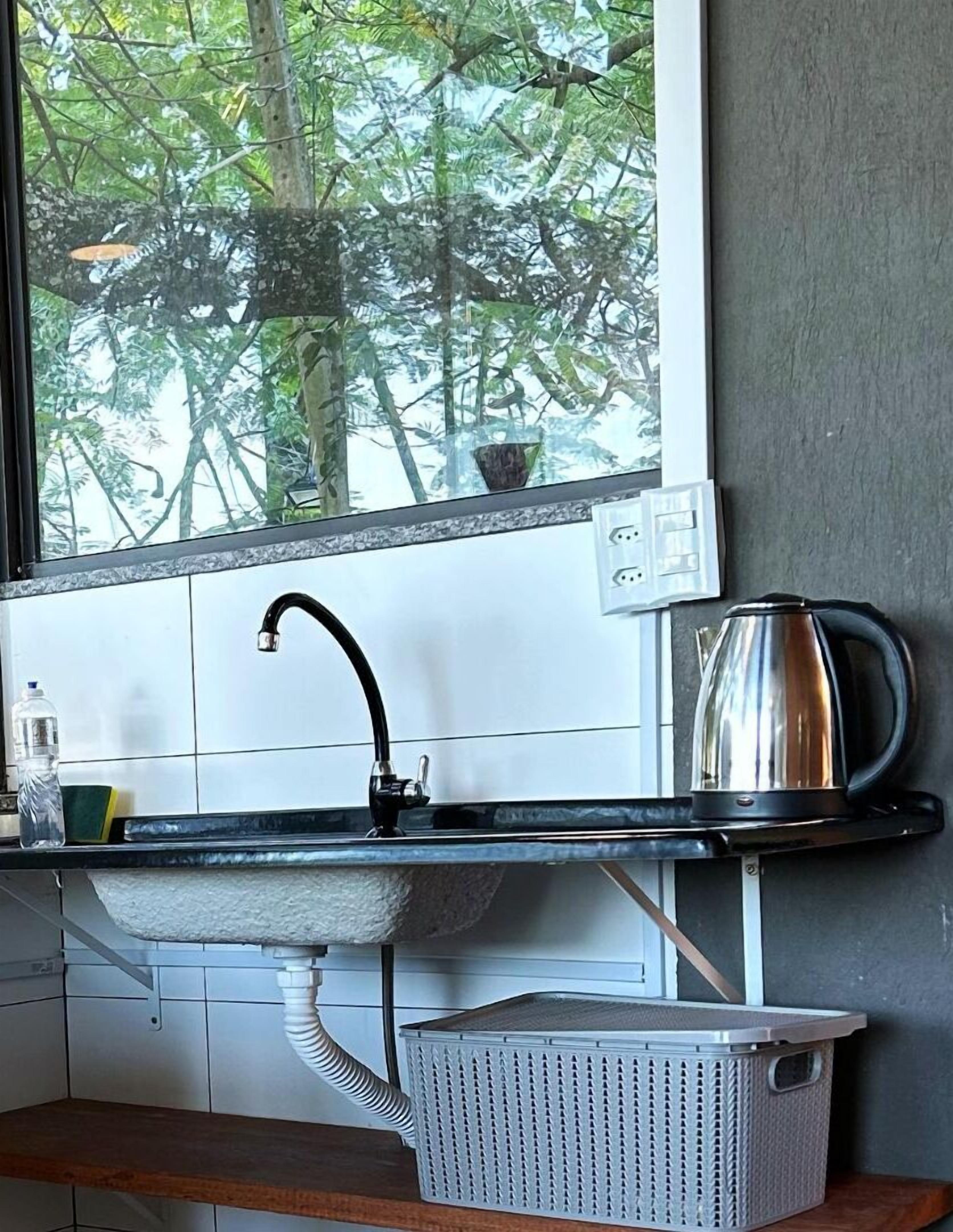 A kitchen with a window, a sink, a kettle, and a basket.
