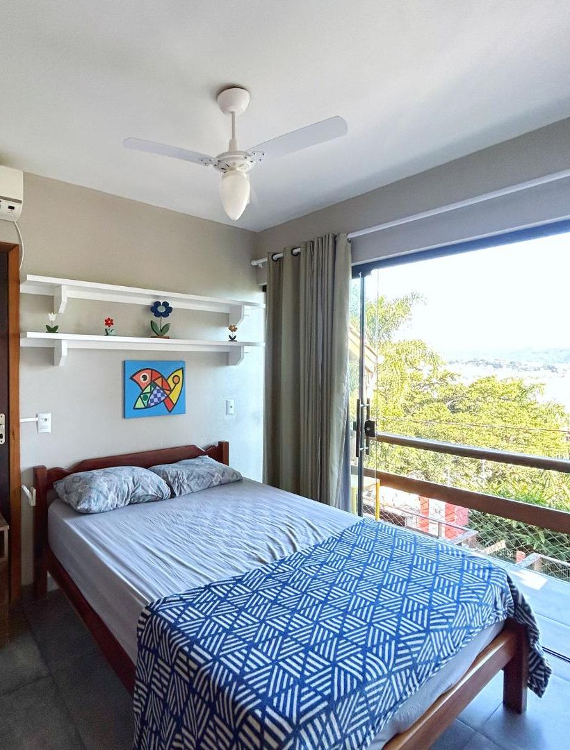 Une chambre à coucher comprenant un lit, un ventilateur de plafond, une fenêtre avec vue et une étagère ornée d’objets décoratifs.
