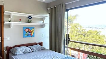 Une chambre à coucher comprenant un lit, un ventilateur de plafond, une fenêtre avec vue et une étagère ornée d’objets décoratifs.