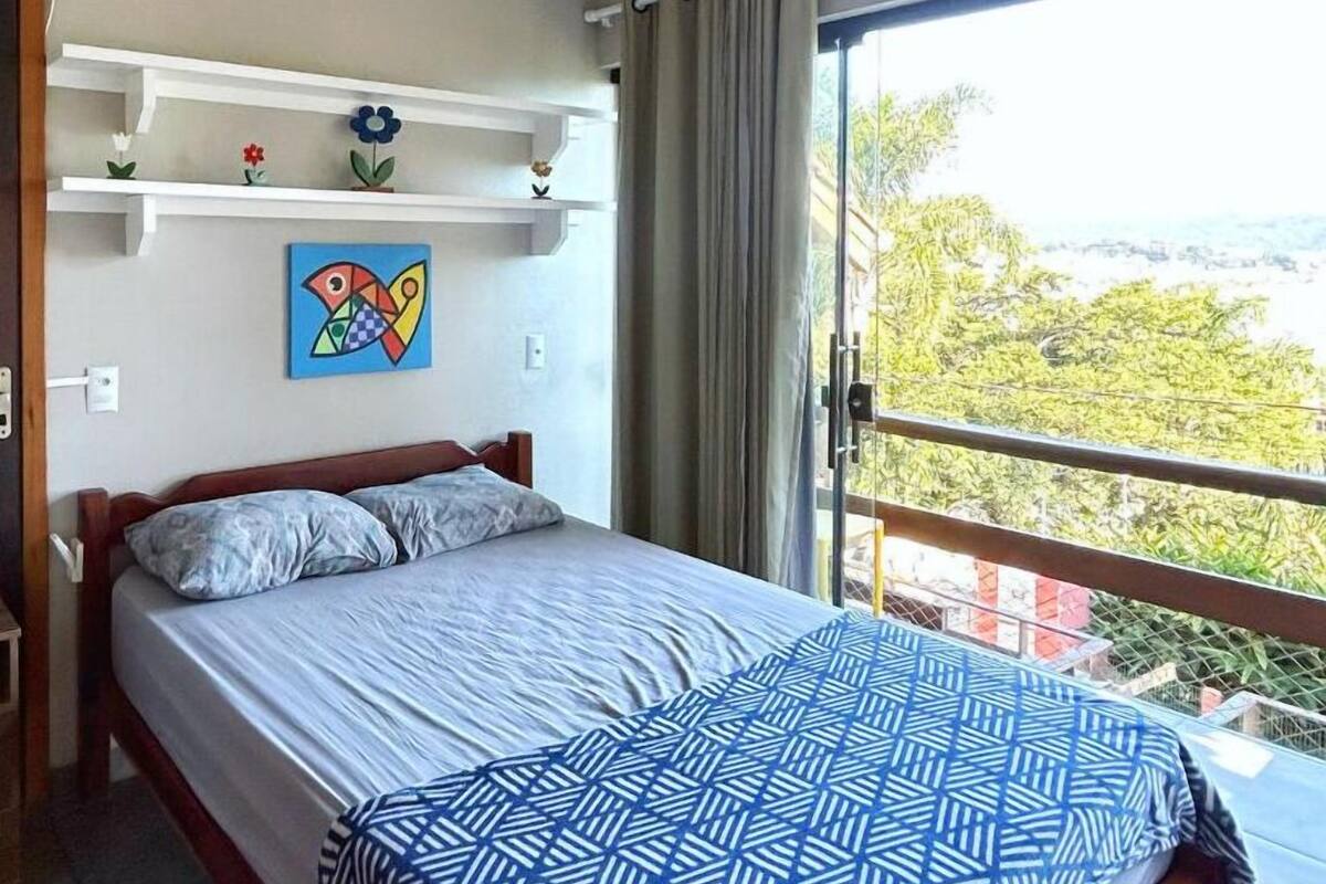 A bedroom with a bed, a ceiling fan, a window with curtains, and a view of greenery.