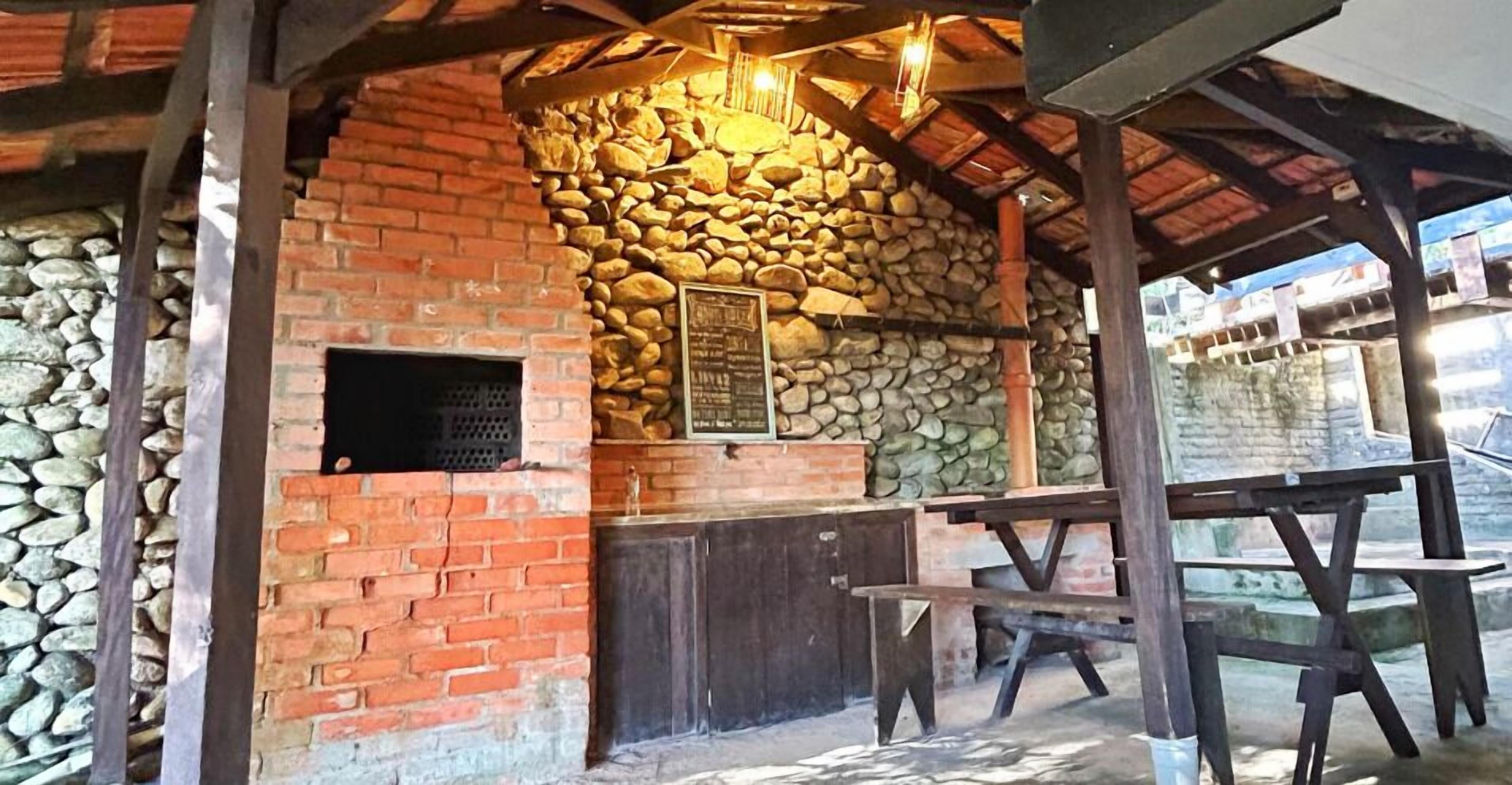 Una estructura rústica de piedra y ladrillo con un banco y una mesa de madera, un muro de piedra y una ventana con marco de metal.