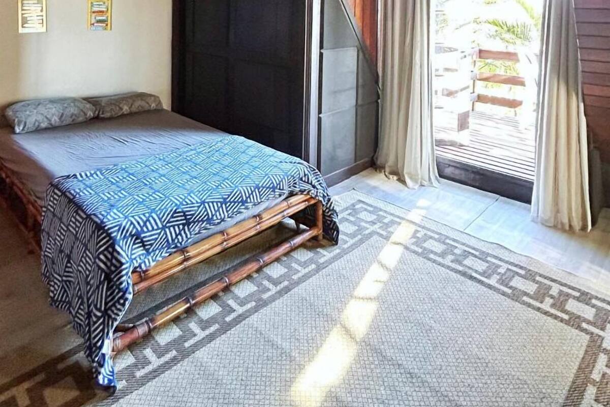 A bedroom with a bed, a ceiling fan, a window with curtains, and a view of the outside.