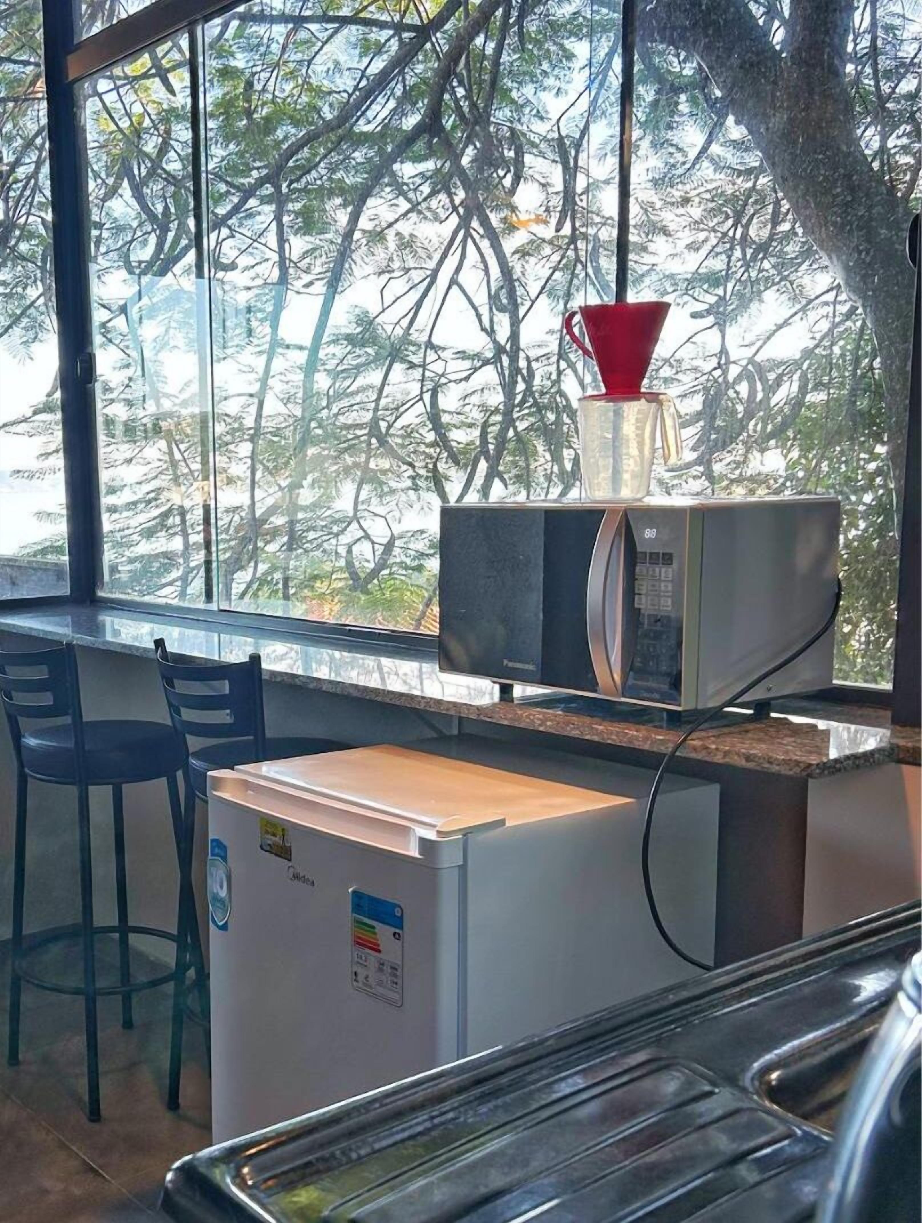 A compact kitchen with a refrigerator, microwave, and a coffee maker on the counter. There are two chairs and a window with a view of trees.