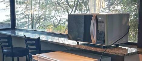 A compact kitchen with a refrigerator, microwave, and a coffee maker on the counter. There are two chairs and a window with a view of trees.