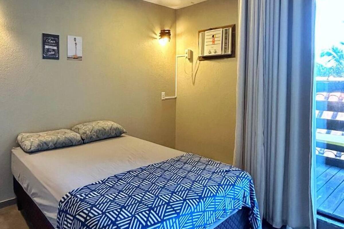 A bedroom with a bed, a ceiling fan, a window with curtains, and a wall-mounted air conditioning unit.