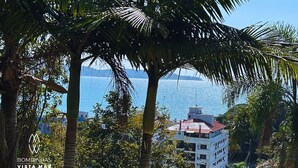 A building with a red roof and white walls, surrounded by palm trees and a clear blue sky. - Bombinhas Vista Mar (Bombinhas)