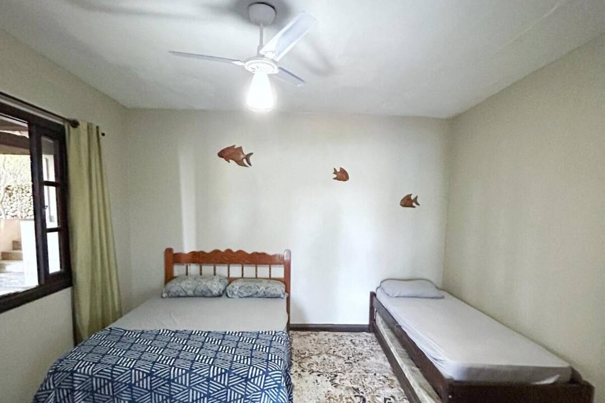 A bedroom with a bed, a smaller bed, a ceiling fan, and a window with curtains.