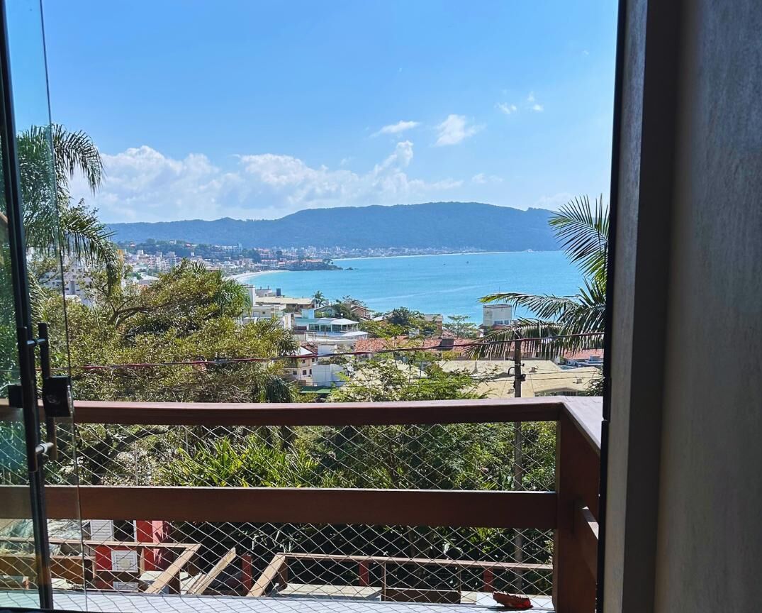 Un balcon offrant une vue sur un paysage urbain côtier, avec une plage et des montagnes à l’horizon.