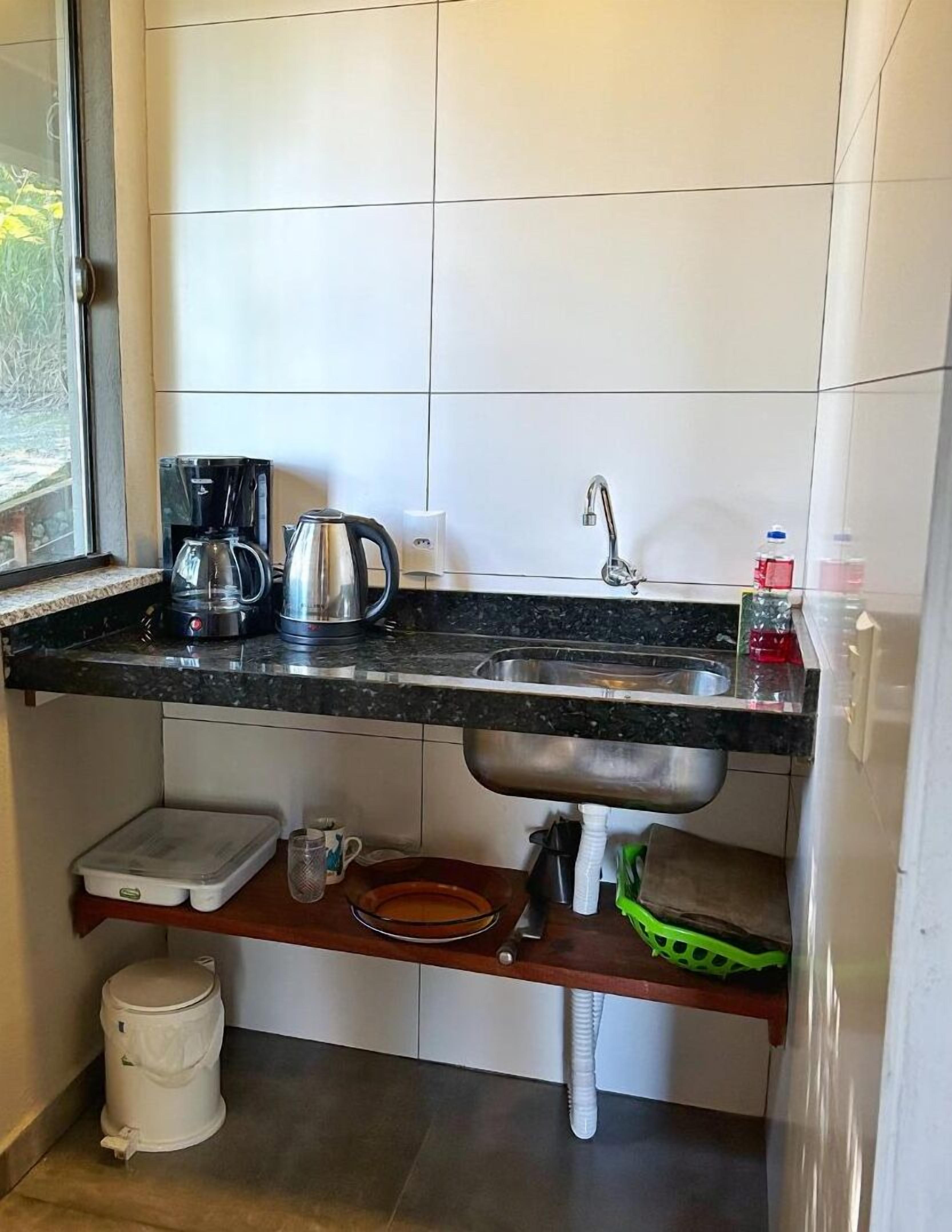 A compact kitchen with a sink, coffee maker, kettle, and a window.
