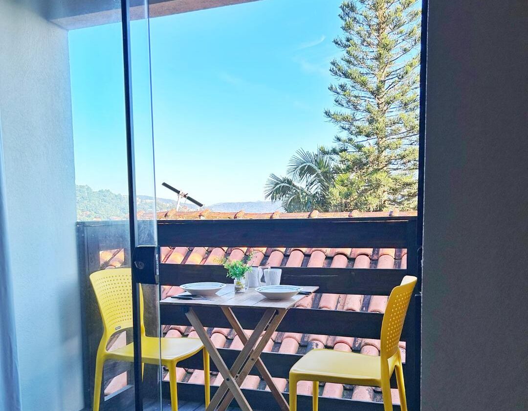 Un balcón con una mesa y dos sillas, con vista a un tejado de baldosas y un árbol.