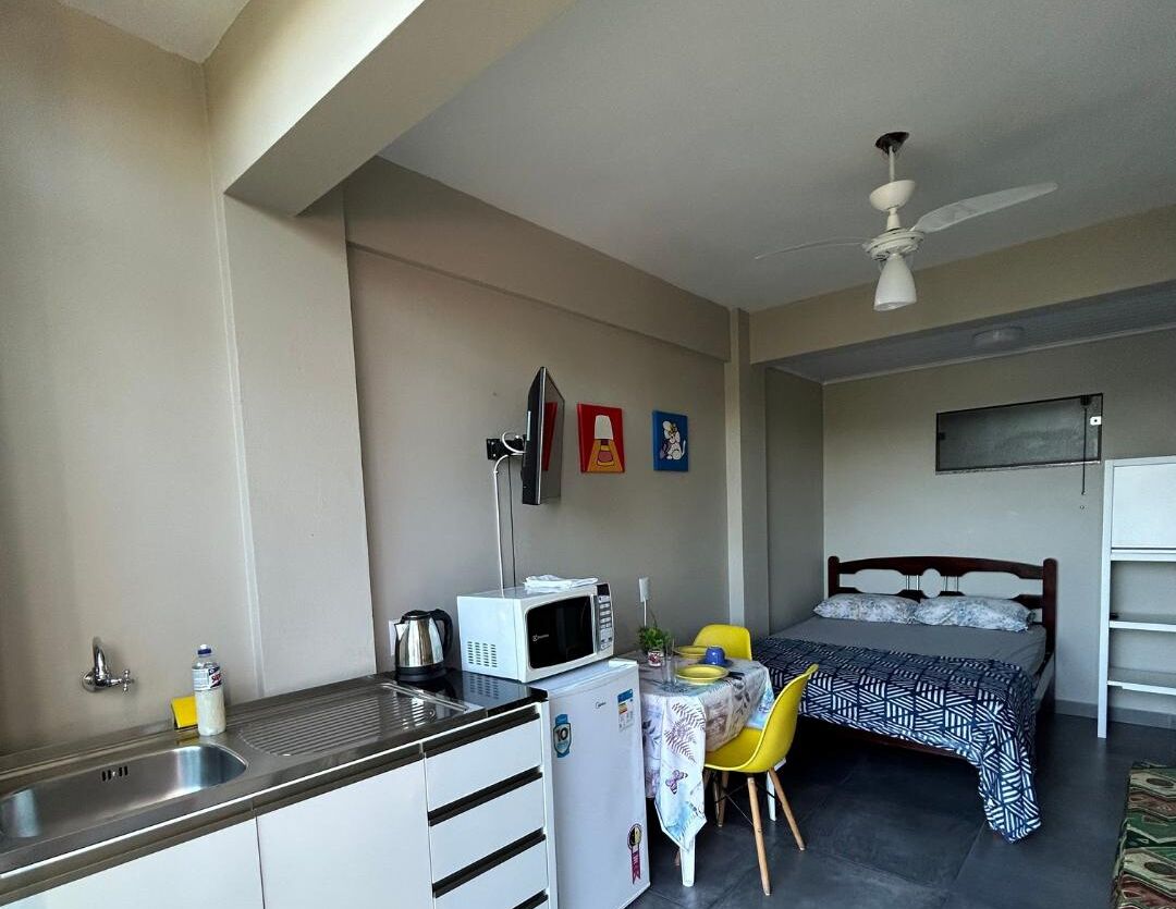 A compact room with a kitchenette, a bed, a table with chairs, and a ceiling fan.