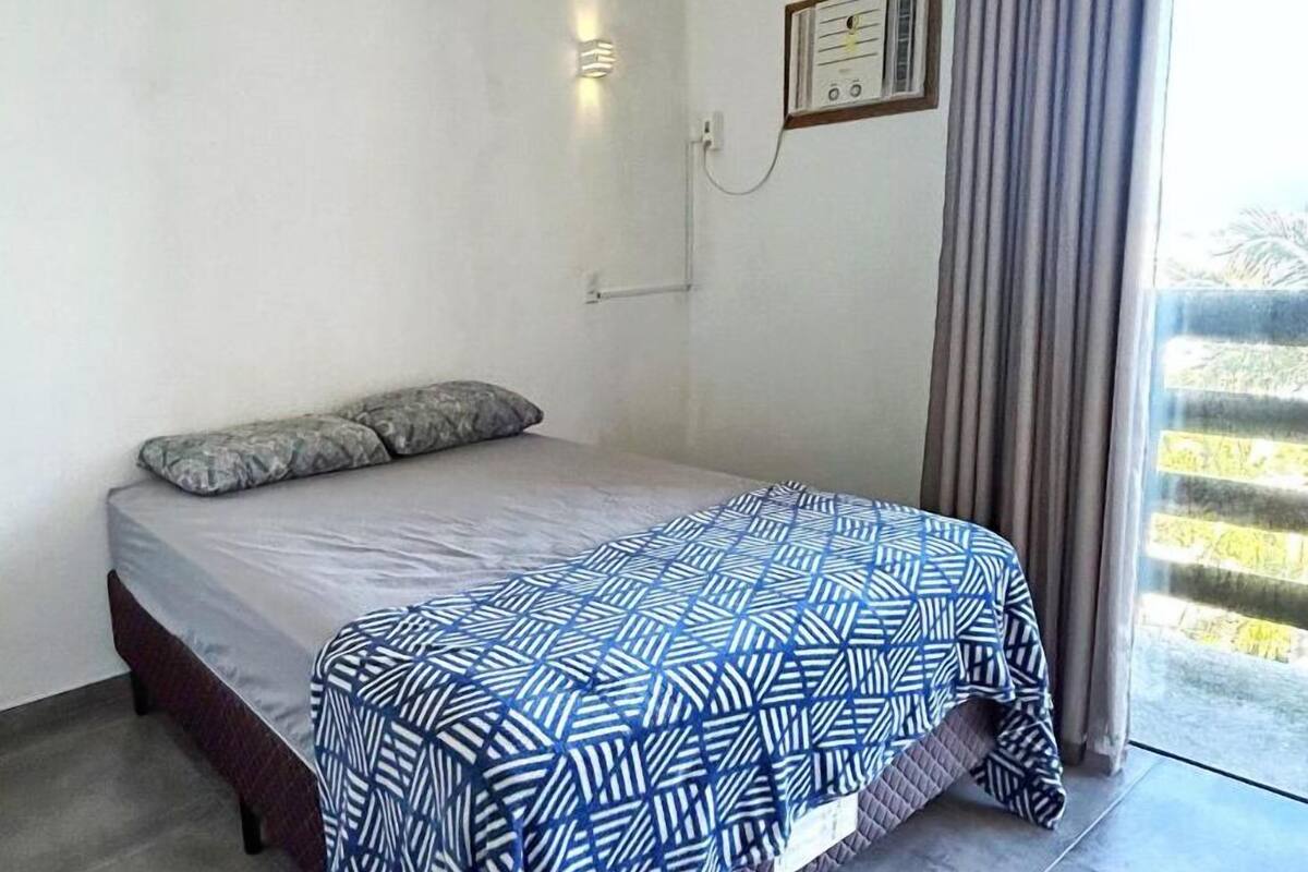 A bedroom with a bed, a ceiling fan, a window with curtains, and a wall-mounted light fixture.