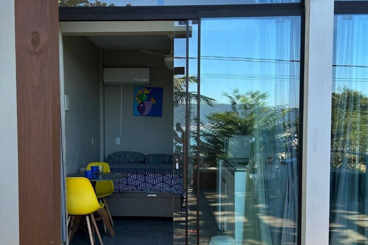 A modern room with a bed, a dining table with chairs, and a glass door leading to an outdoor area.