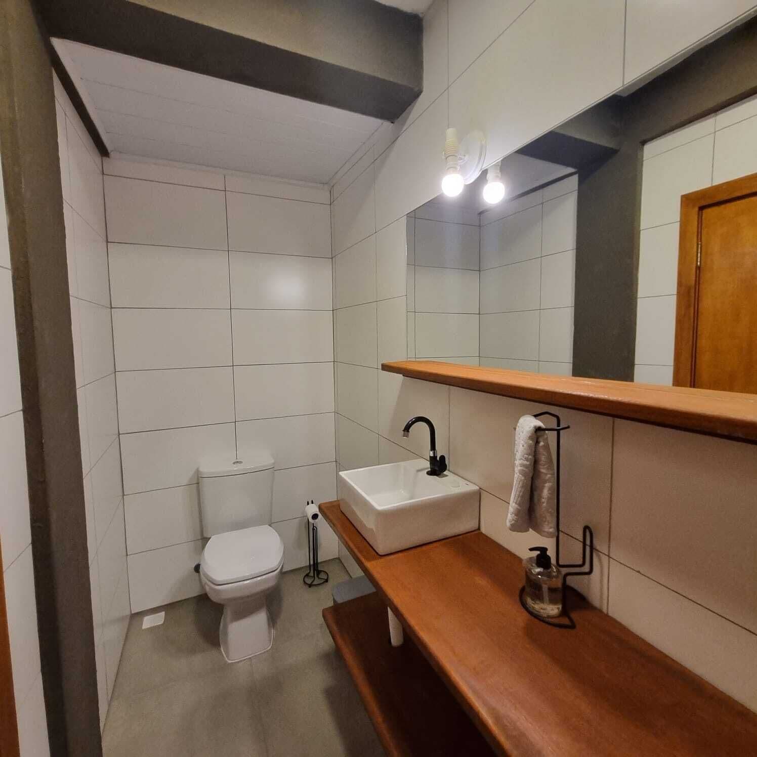 Een moderne badkamer met witte tegels, een wit toilet, een houten wastafelmeubel met een wastafel, een spiegel en een handdoekhouder.