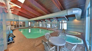 An indoor swimming pool with a wooden ceiling, a table with chairs, and a jacuzzi.