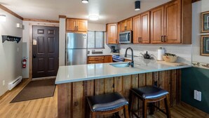 A modern kitchen with wooden cabinets, a stainless steel refrigerator, a microwave, and a large island with two stools.