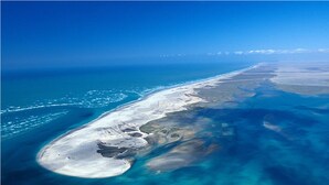 An aerial view of a coastal area with clear blue waters, sandy beaches, and a long stretch of land.