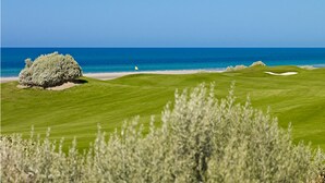A golf course with a clear view of the ocean and a flag marking a hole.