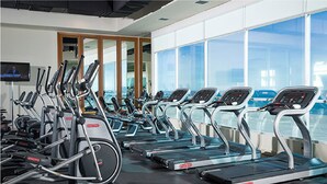 A gym with multiple treadmills, exercise bikes, and a television screen.