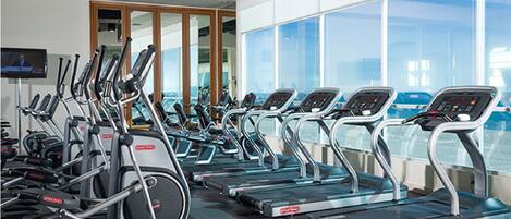 Et fitnesscenter med flere løbebånd, træningscykler og et fjernsyn.