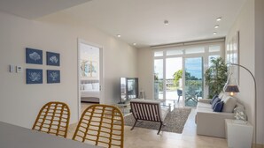 Un salon moderne comprenant un coin repas, un canapé et un téléviseur. Il y a également un balcon avec vue sur l’extérieur.