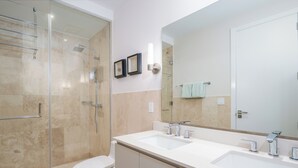 Une salle de bain moderne avec une douche à l’italienne en verre, des toilettes blanches et un meuble-lavabo double doté d’un grand miroir.