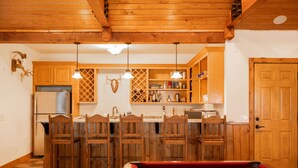 Una mesa de billar en una habitación con muebles de madera y una zona de cocina con armarios de madera y un refrigerador.