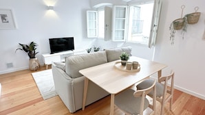 A modern living room with a sofa, a dining table with chairs, a TV, and a hanging light fixture. - Bombarda 15 Evora (Évora)