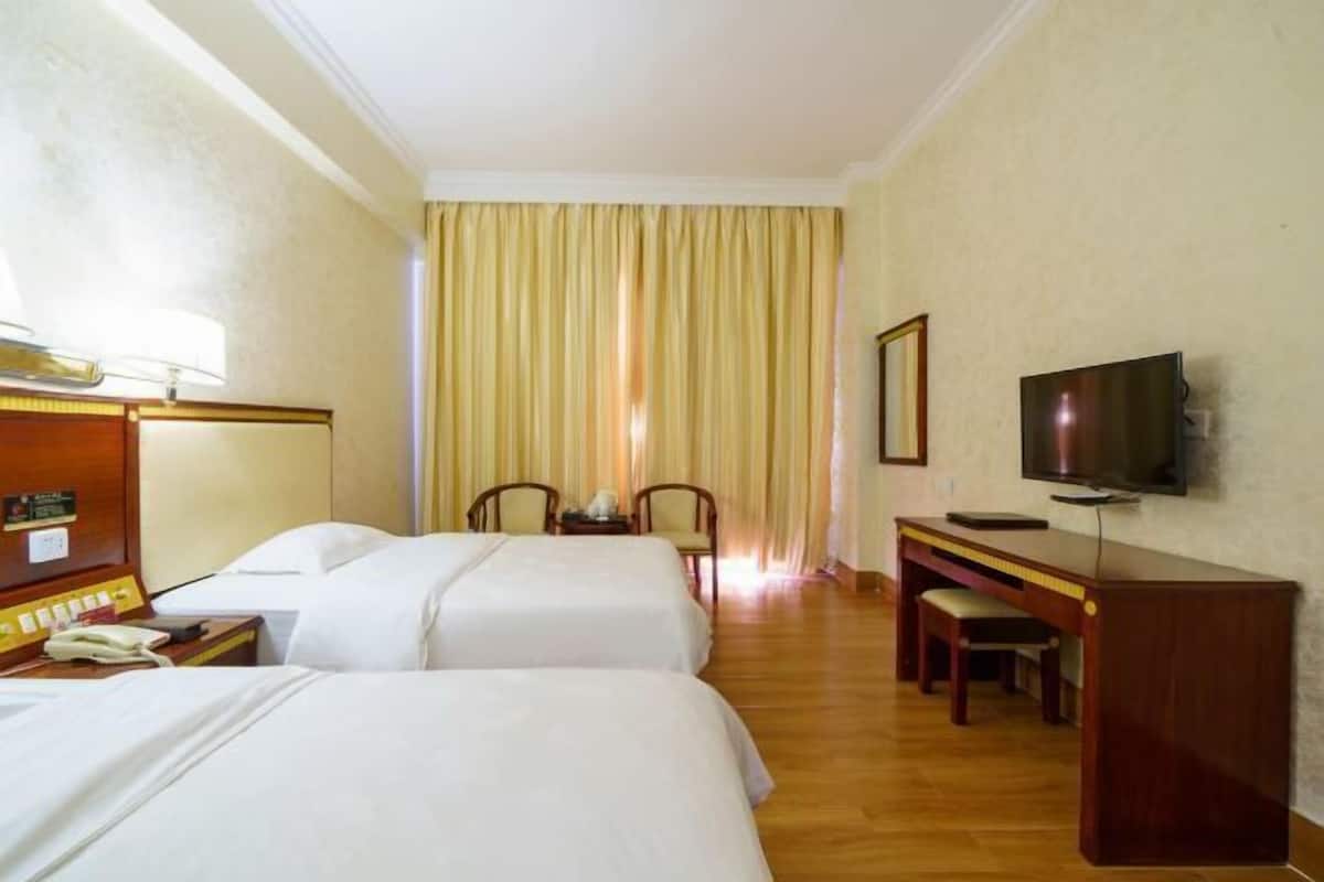 Quarto de hotel com duas camas, uma escrivaninha, uma TV e uma cadeira.