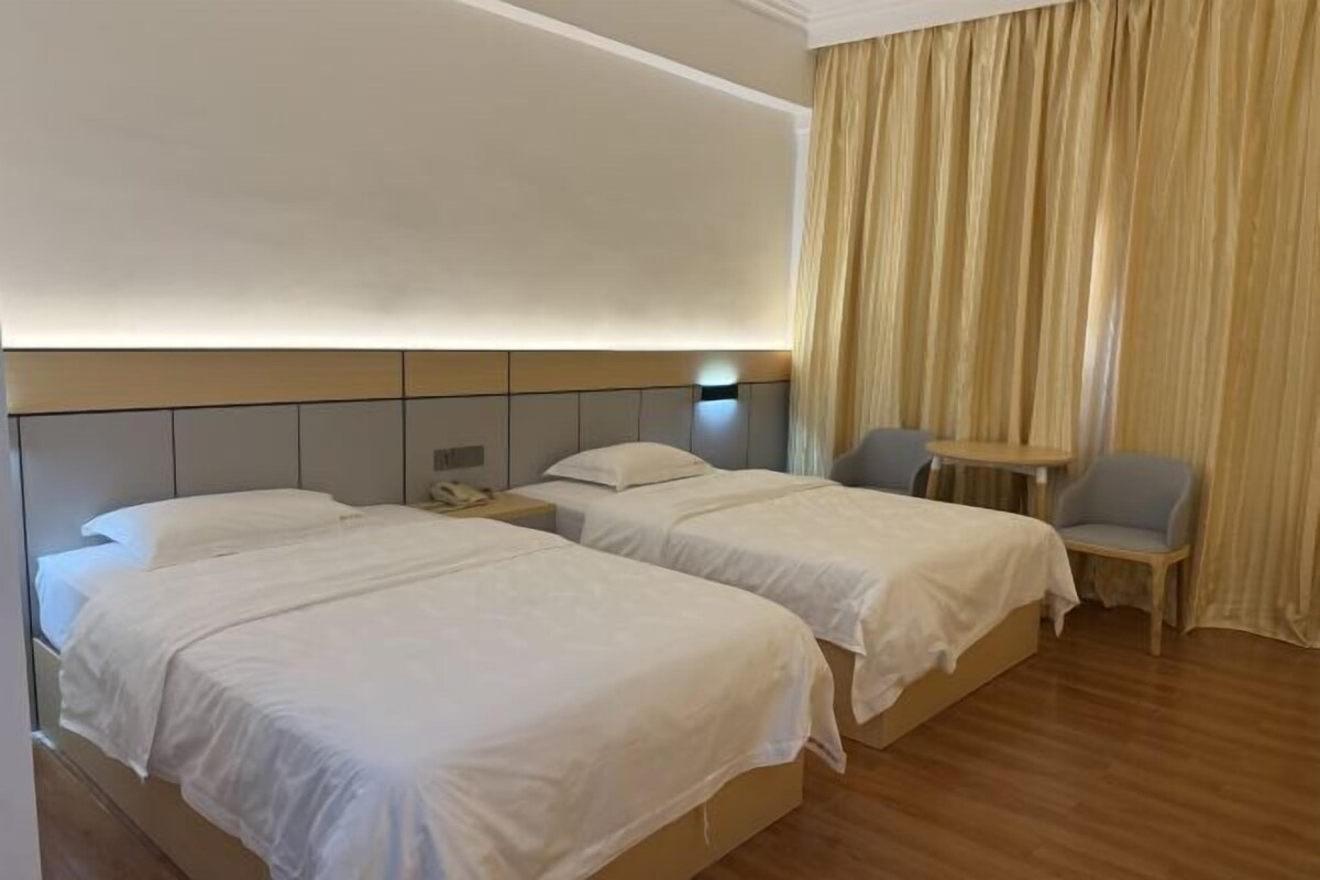 Habitación de hotel con dos camas, una mesita, una silla y una cortina.