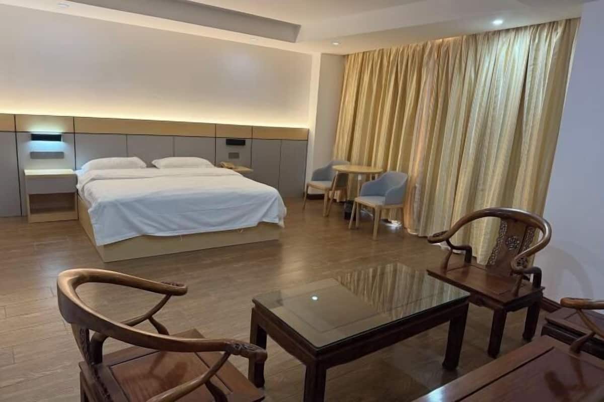 Quarto de hotel com cama, mesas de cabeceira, uma mesa com tampo de vidro, duas cadeiras e cortina.