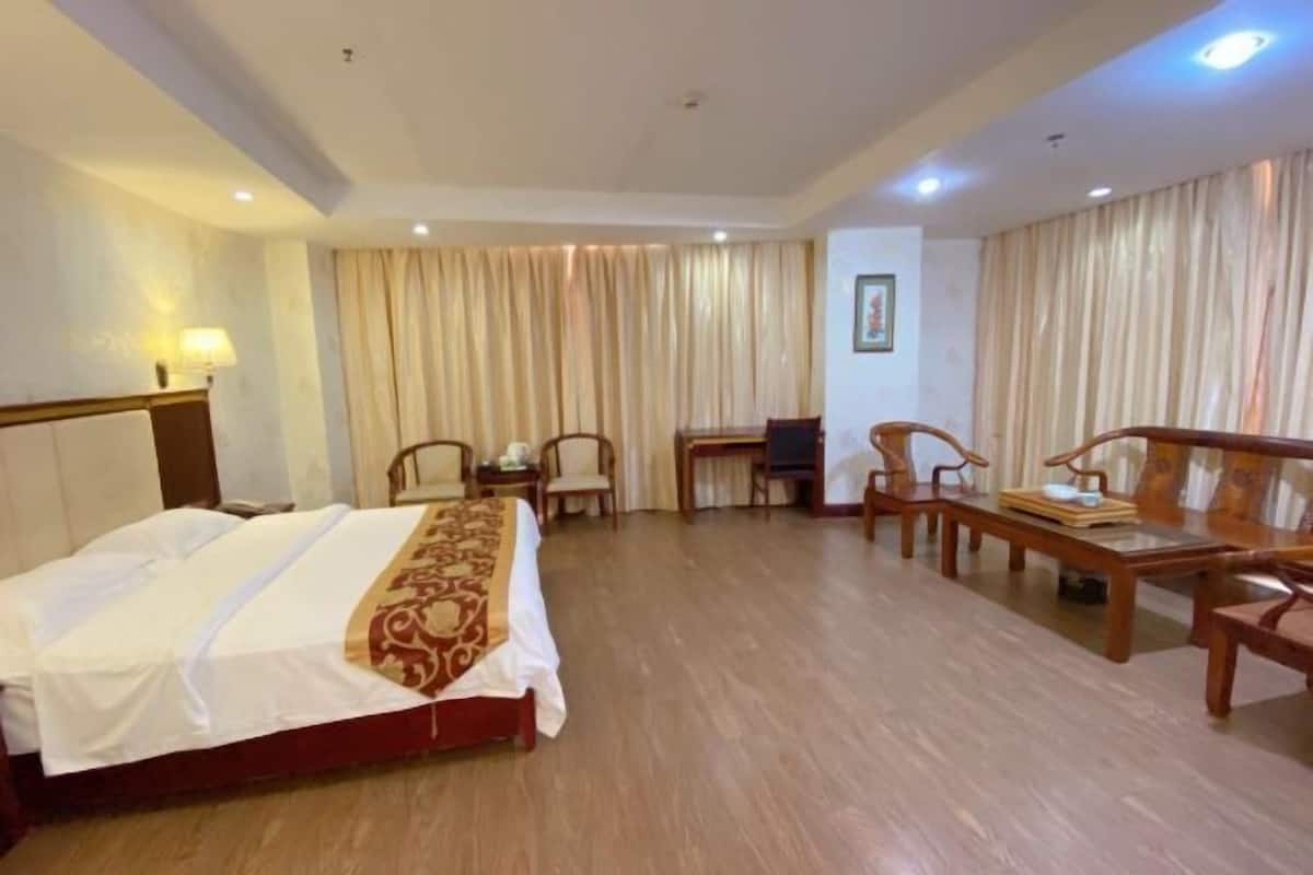 Quarto de hotel com cama, escrivaninha, duas cadeiras, televisão e cortinas.
