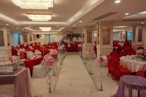 Un salón de banquetes con mesas redondas, sillas rojas y un pasillo central.