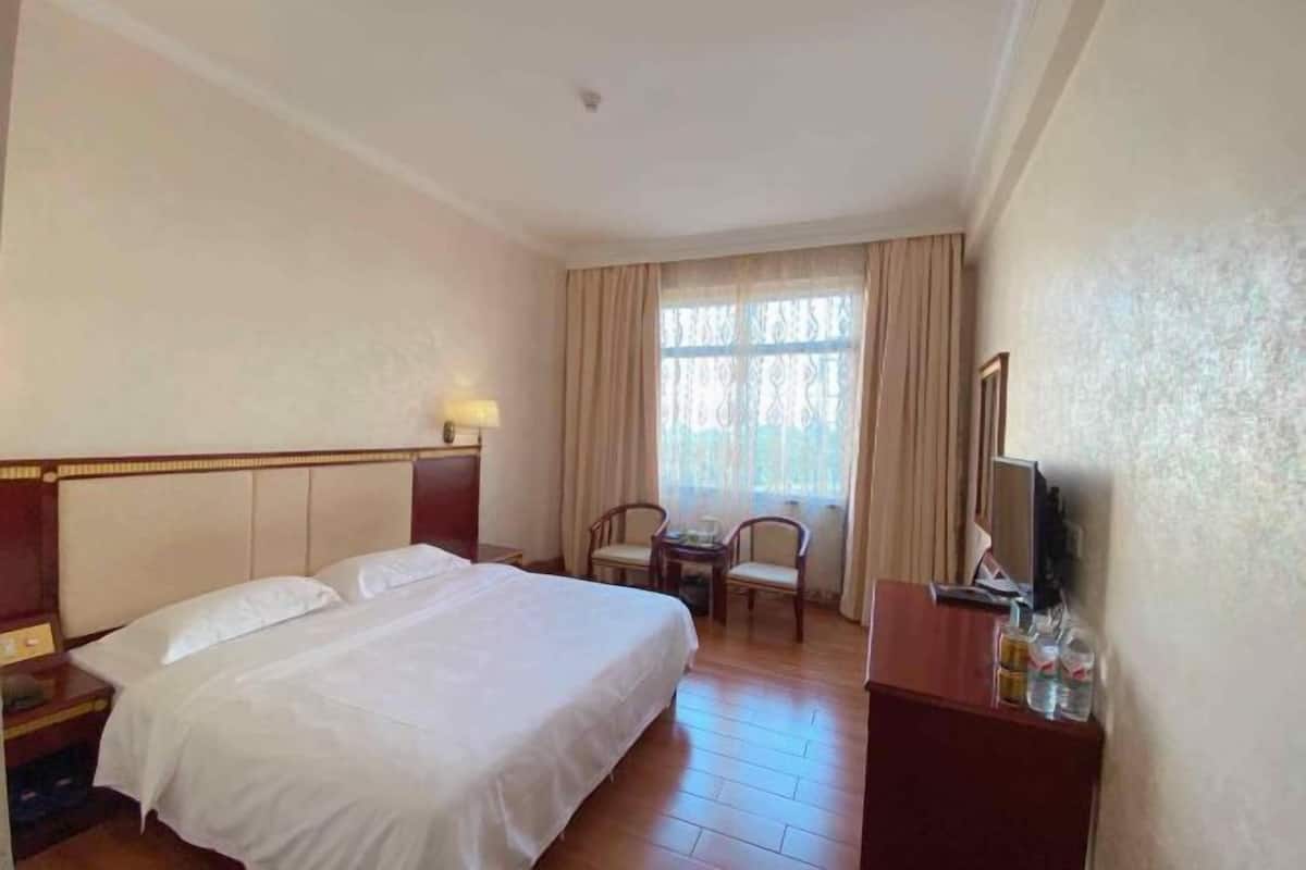 Quarto de hotel com uma cama grande, uma escrivaninha com cadeira, televisão e uma janela com cortinas.